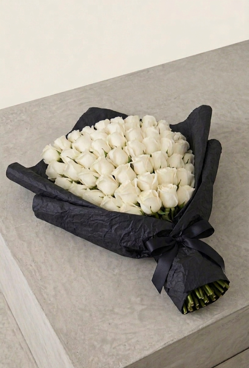 Bouquet of white roses wrapped in black paper on a light gray surface